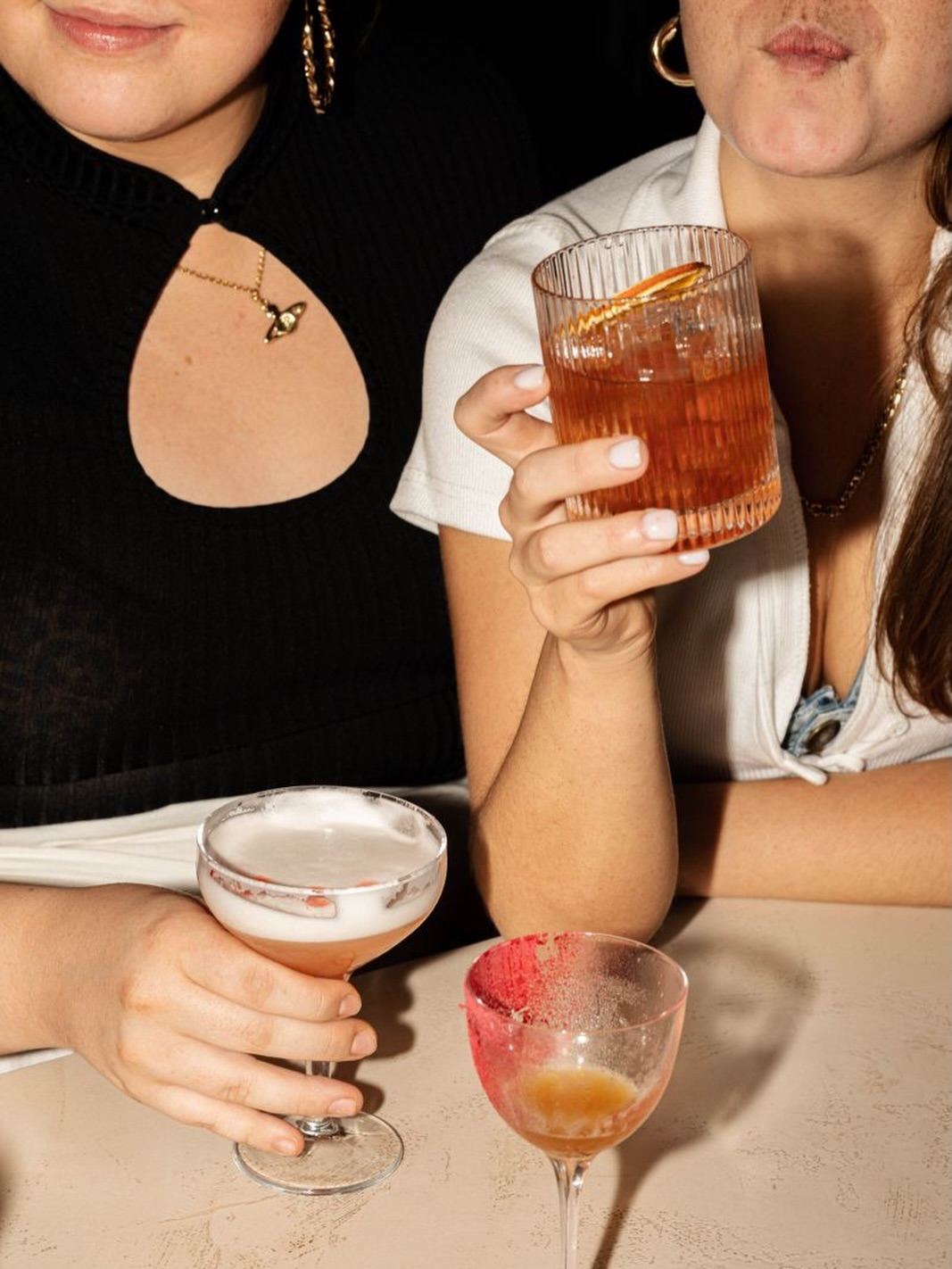 Due amiche al bancone con un cocktail e un sour in mano