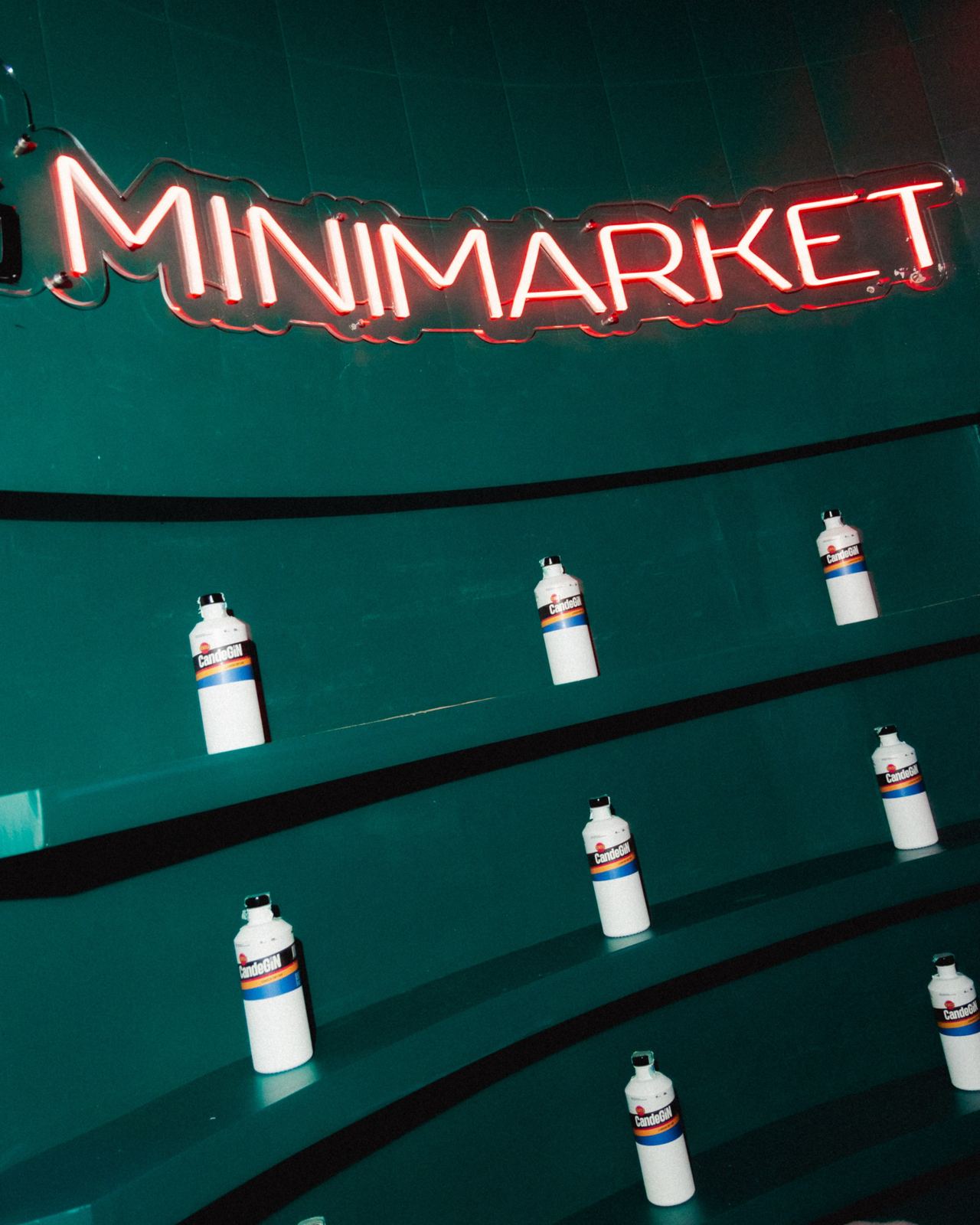 Insegna Minimarket al neon rosso sulla parete verde, con le bottiglie sugli scaffali