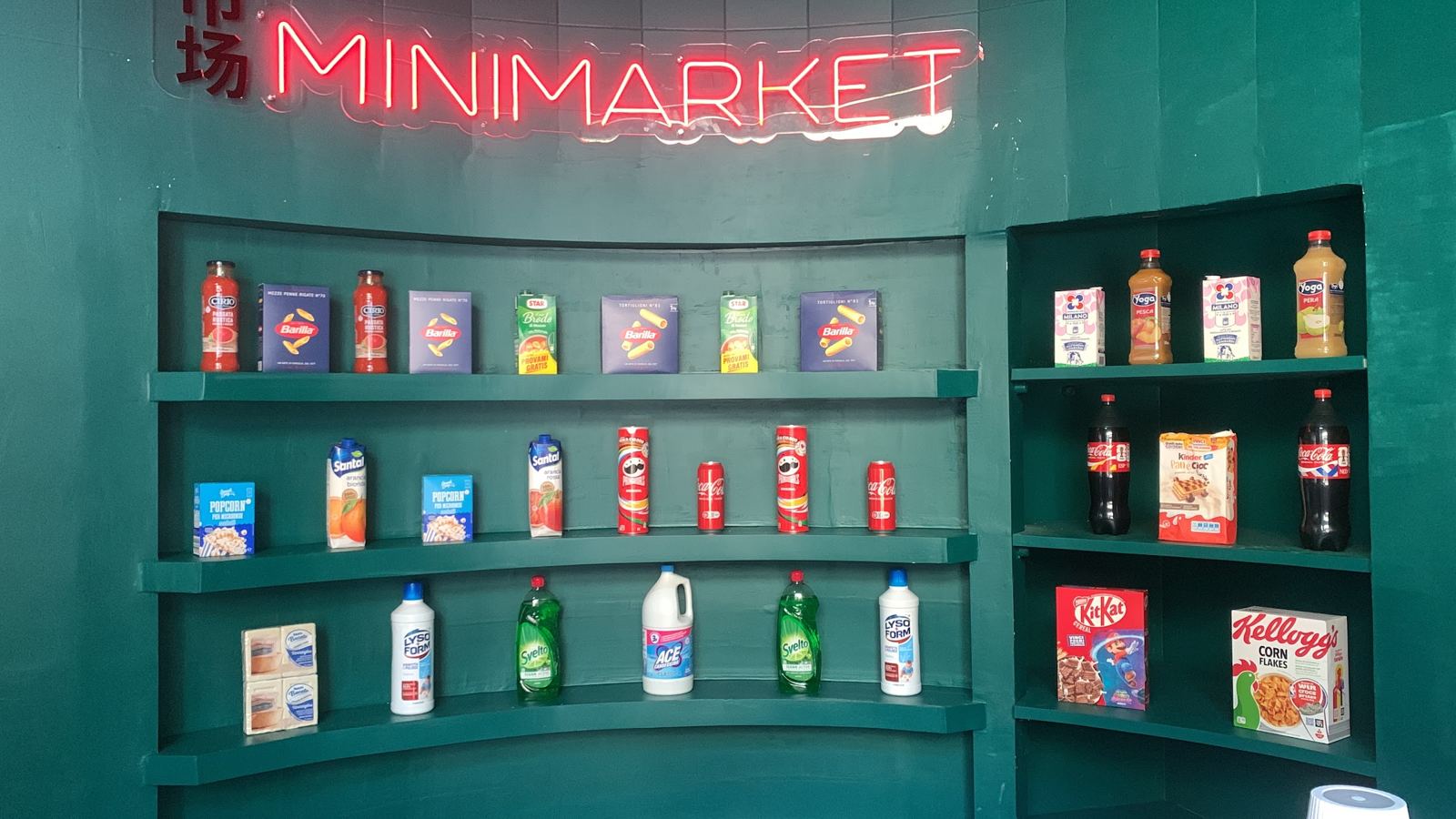 La parete verde con l'insegna Minimarket al neon e gli scaffali pieni di prodotti da minimarket